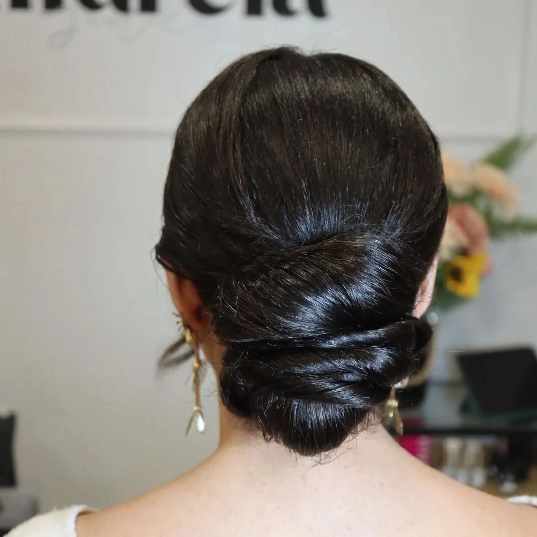 Smooth dark hair folded into a compact low nape updo