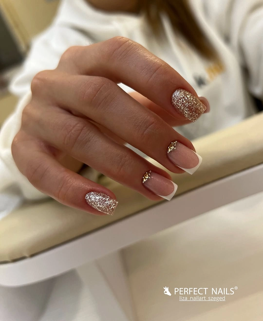 Pink square French tip nails with sparkling glitter and small gold accents