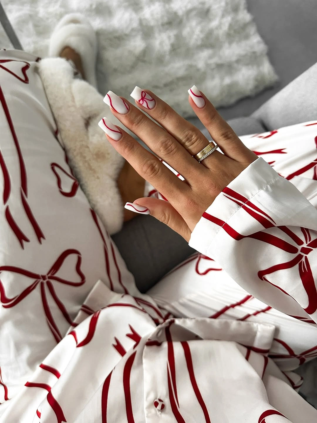 Creamy white rounded nails with sweeping red lines and a small bow
