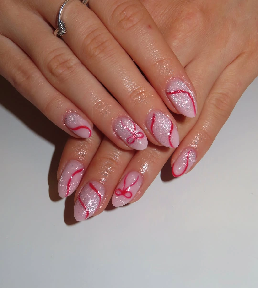 Shimmering pale pink almond nails with curved red stripes and tiny bows