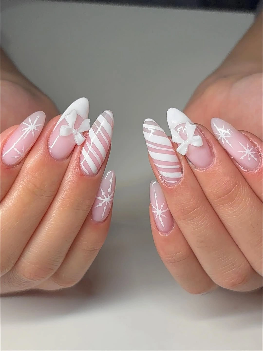 Long pink almond nails with white bows, snowflakes, and diagonal stripes