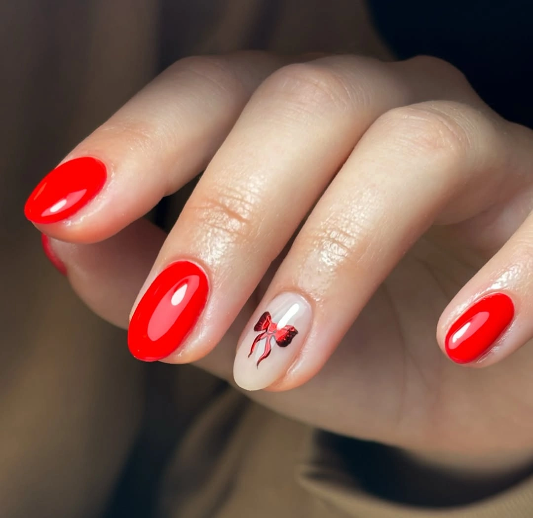Glossy rounded red nails with one pale accent and red bow