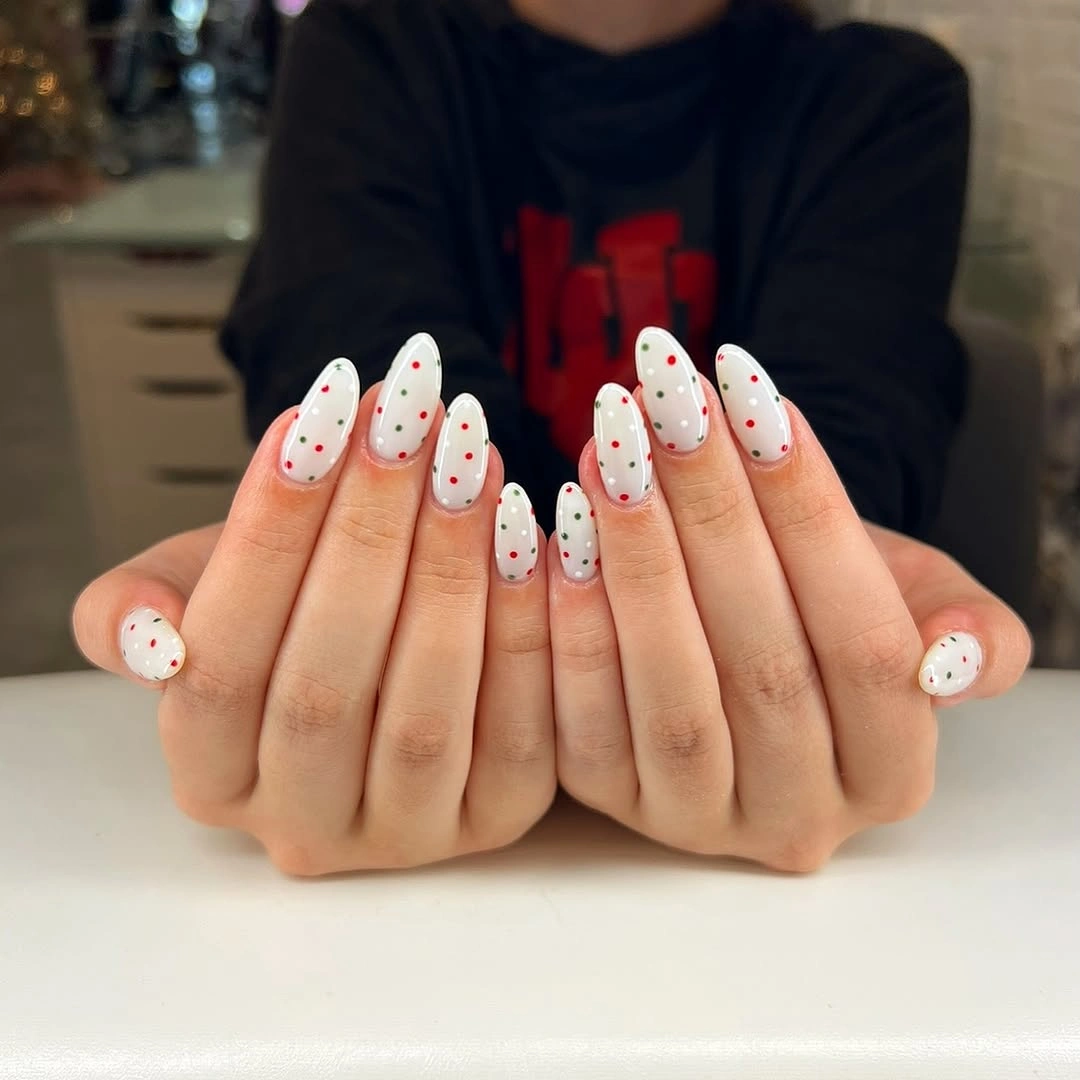 Long white almond nails with scattered red and green dots on both hands