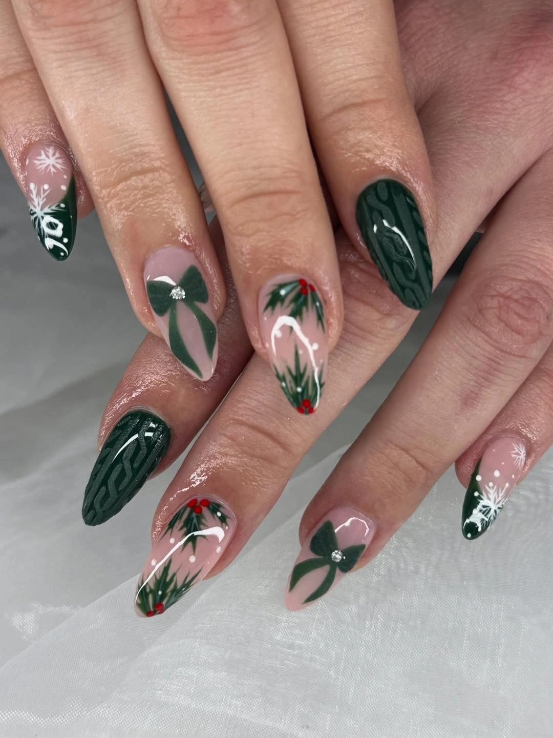 Long almond nails with dark green cable patterns, pink panels, and bows