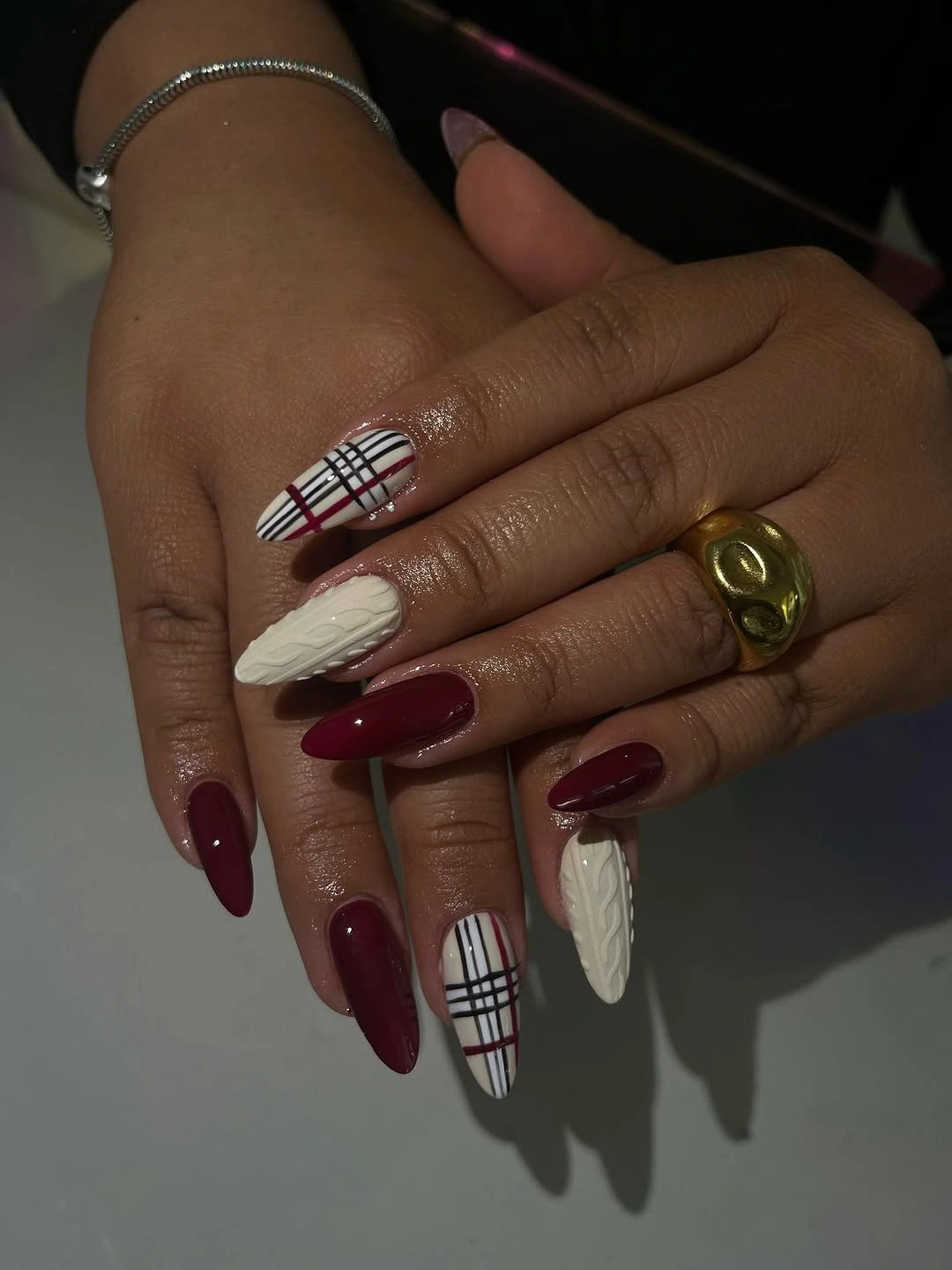 Long almond nails with burgundy polish, cream cable texture, and red plaid