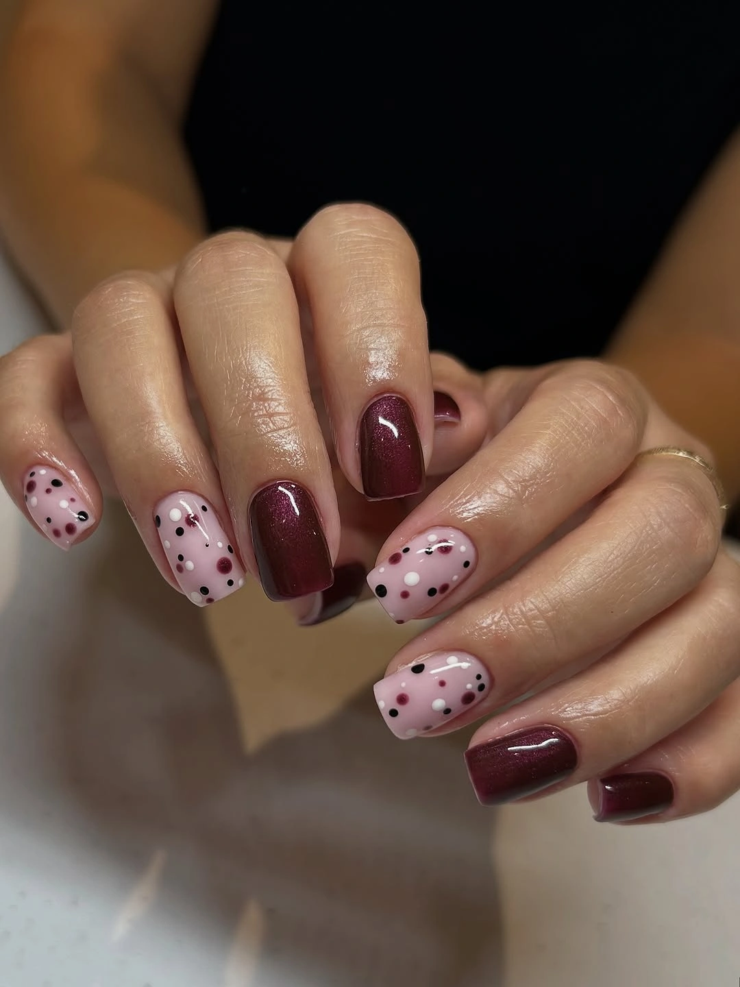 Rounded-square burgundy nails with pale pink accents covered in small dots
