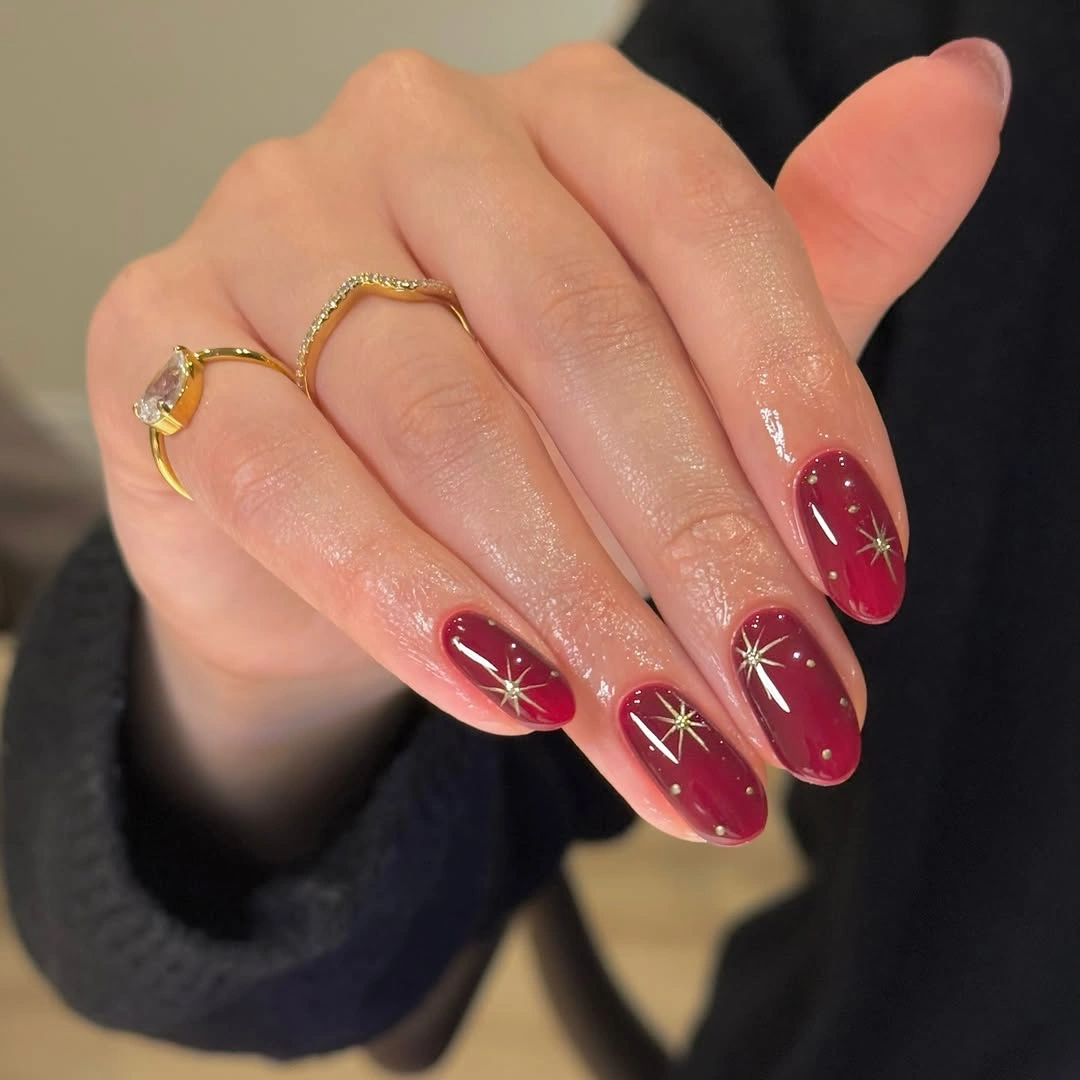 Glossy burgundy almond nails decorated with fine gold stars and dots