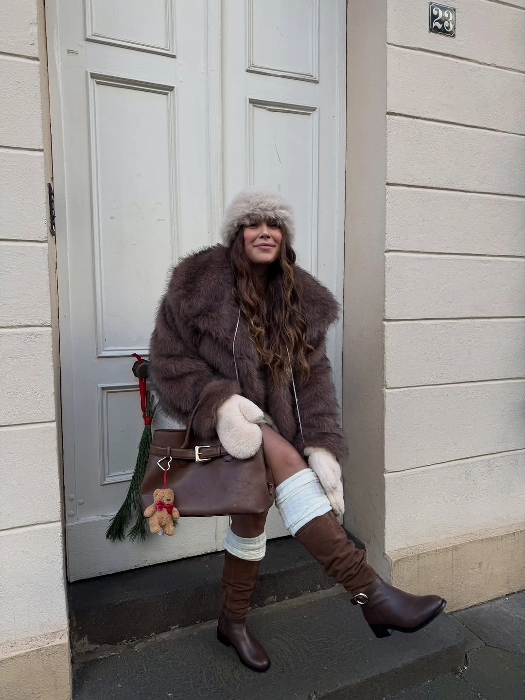 Woman in plush brown jacket, pale hat, mittens, and tall boots