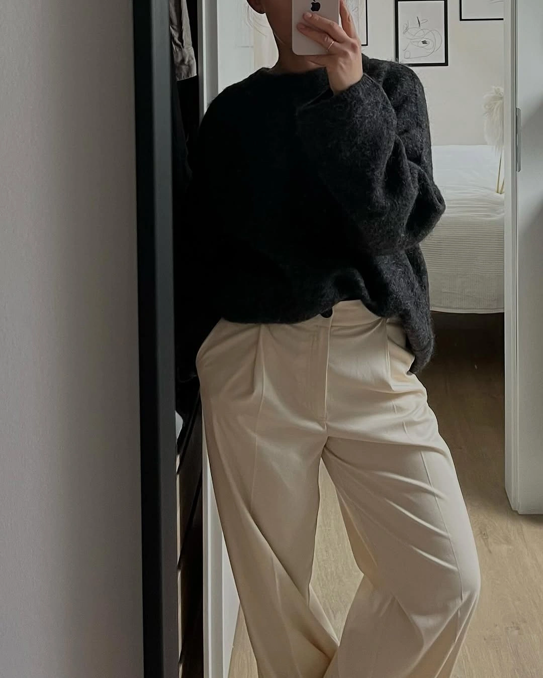 Woman in oversized charcoal sweater and pleated cream trousers indoors