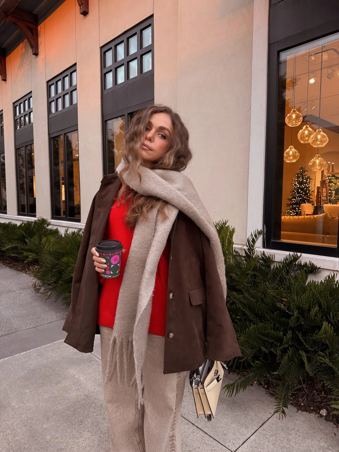 Woman in red sweater, brown blazer, pale scarf, and beige trousers