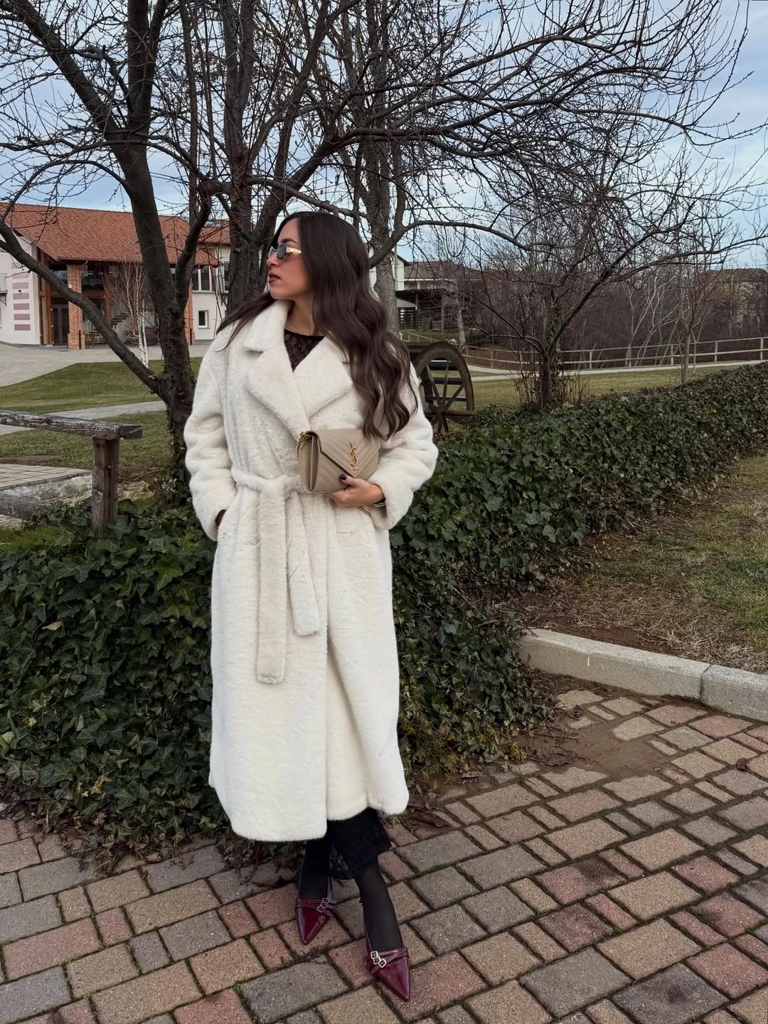 Woman in long cream wrap coat with burgundy pointed shoes and clutch