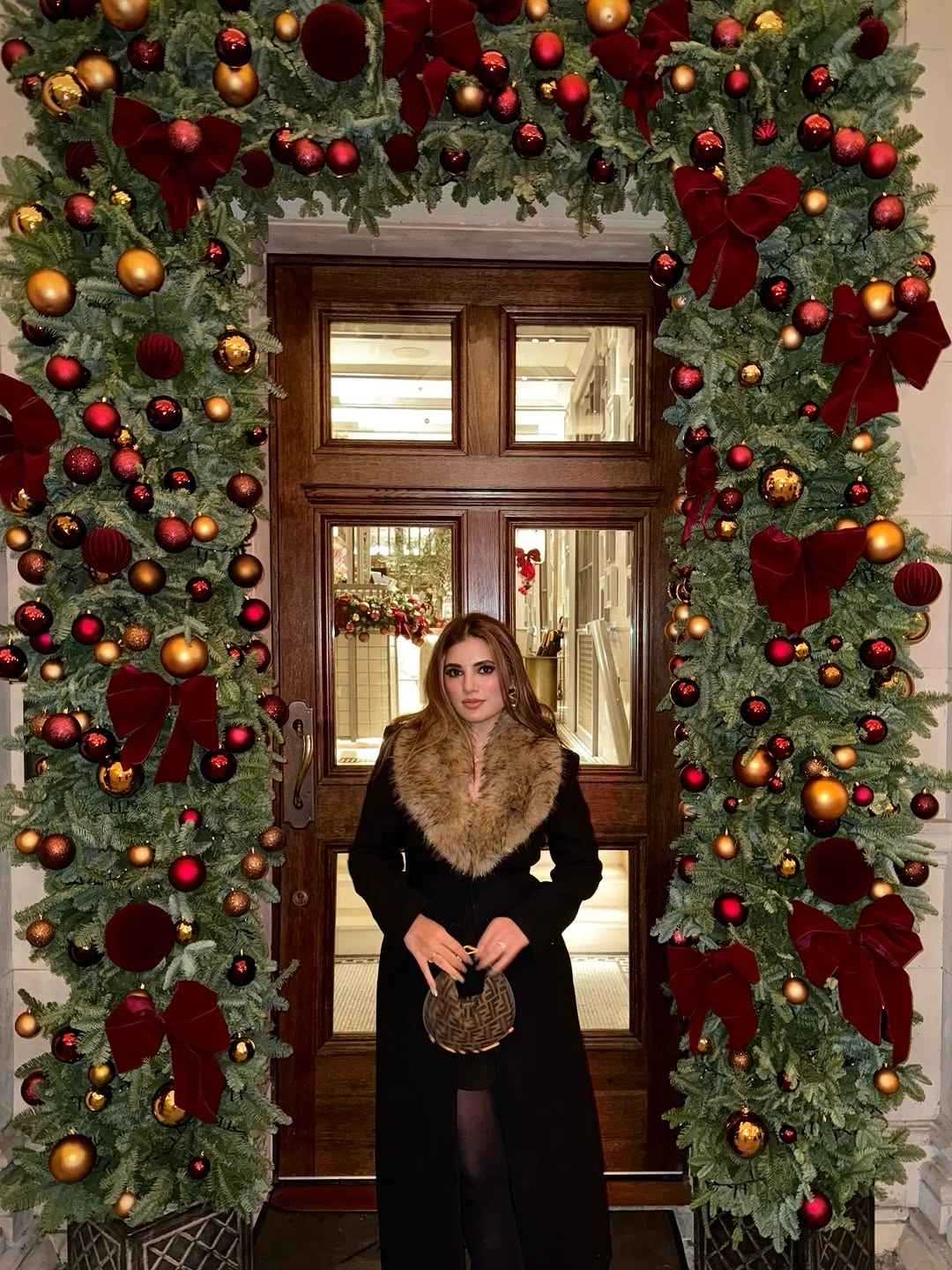 Woman in long black coat with tan plush collar and patterned handbag