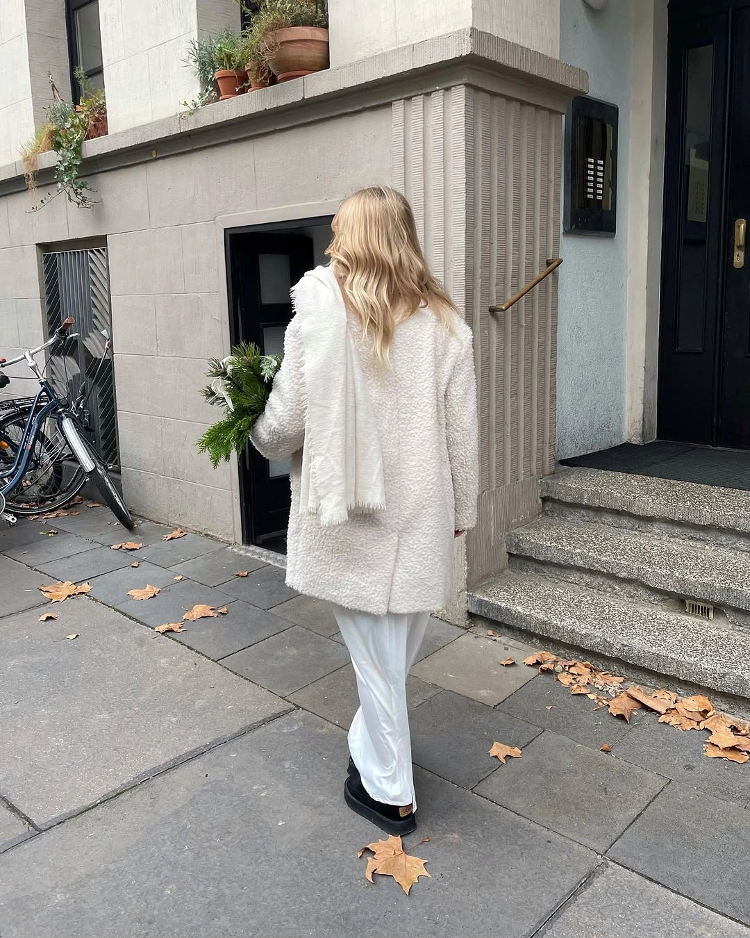 Woman wearing textured white coat, hanging scarf, light trousers, and black shoes