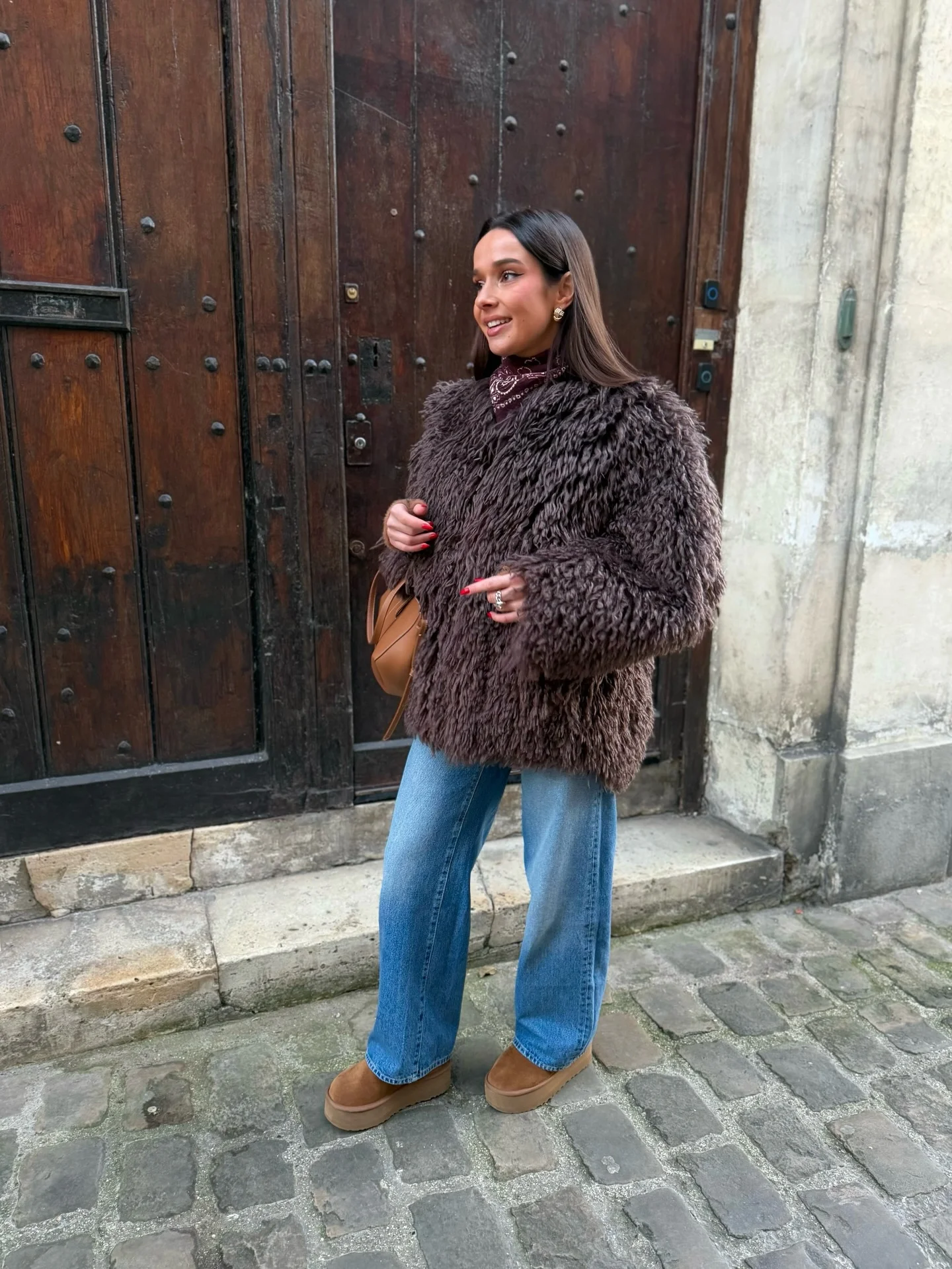 Woman in shaggy brown jacket, wide jeans, tan shoes, and shoulder bag
