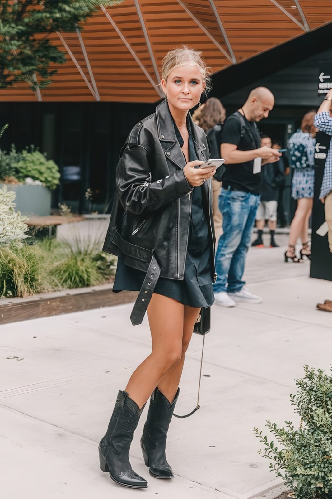 Black Leather Cowboy Boots with Mini Dress and Oversized Jacket — Trendy Black Cowboy Boots Outfit